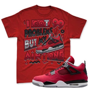 May include: Red t-shirt with the text "I Got 99 Problems But My Ain't One" and a graphic of a red and black sneaker. A matching red and black sneaker is in the foreground.