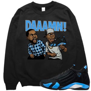 May include: Black sweatshirt featuring a cartoon graphic of two men with the word "DAAAMN!" in blue. A pair of black and blue sneakers are displayed below the sweatshirt, showcasing a sporty aesthetic.