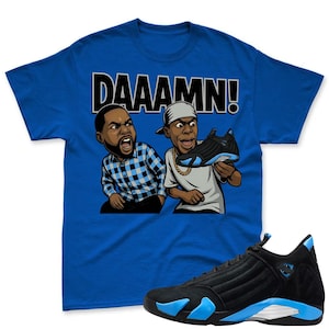 May include: Royal blue t-shirt with the word "DAAAMN!" in white block letters. The shirt features a cartoon graphic of two men, one holding a black and blue sneaker. A black and blue sneaker is in the foreground.