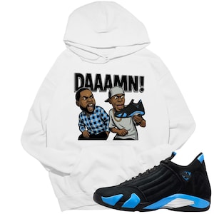 May include: White hoodie with a graphic of two cartoon characters and the word "DAAAMN!". A black and blue sneaker is in the foreground. The hoodie features a drawstring hood and a kangaroo pocket.
