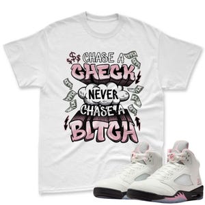 May include: White t-shirt with the text "Chase a Check Never Chase a Bitch" in a graffiti-style design with dollar signs and money graphics. White and pink sneakers are in the foreground.
