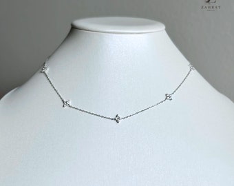 Puede incluir: Un collar de cadena de plata con cuatro pequeños colgantes en forma de diamante. Cada colgante está hecho de pequeñas piedras brillantes.