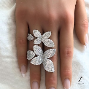 Puede incluir: Un anillo de plata con un diseño floral que presenta múltiples formas de flores engastadas con piedras de circonita cúbica transparentes.