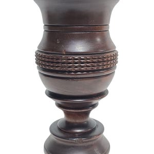 Könnte beinhalten: Eine dunkelbraune Holzvase mit breitem Oberteil und einem dekorativen, geschnitzten Band in der Mitte. Die Vase hat einen Sockel und eine glatte, polierte Oberfläche. Die Vase ist ein dekorativer Einrichtungsgegenstand.
