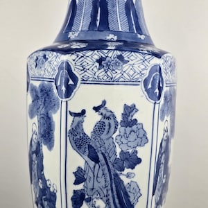Puede incluir: Un jarrón de cerámica alto, azul y blanco, con un diseño detallado pintado a mano. El jarrón presenta un patrón repetido de hojas estilizadas y motivos florales. El panel central representa dos pájaros y un arreglo floral. El jarrón mide aproximadamente 46 cm de alto.