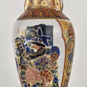 Könnte beinhalten: Eine dekorative Keramikvase mit detailliertem Blumen- und Vogeldesign. Die Vase hat einen weißen Körper mit bunten Blumen, Vögeln und goldenen Akzenten. Der obere und untere Teil haben einen goldenen Rand mit einem rot-goldenen Muster.