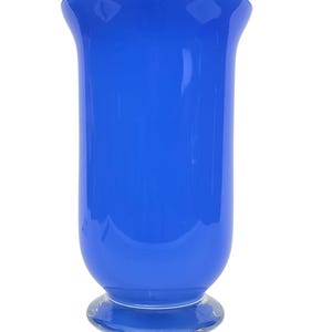 Puede incluir: Un jarrón de vidrio azul vibrante con una parte superior acampanada y una base redondeada. El jarrón tiene un acabado liso y brillante y se asienta sobre una base clara y circular. Esta pieza decorativa es ideal para exhibir flores o como acento independiente.