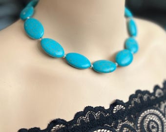 Puede incluir: Un collar turquesa con grandes cuentas ovaladas. El collar se exhibe en un maniquí, resaltando el vibrante color azul-verdoso de las piedras. Las cuentas están ensartadas con conectores plateados, creando un contraste llamativo.
