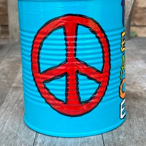 May include: A turquoise painted tin can with a red peace sign and the words "Peace Love & Cookies" in rainbow colors.