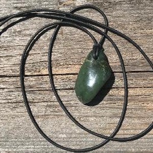 May include: A dark green jade pendant on a black leather cord. The pendant is smooth and oval-shaped.