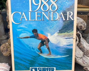 May include: A vintage 1988 calendar featuring a surfer riding a wave. The calendar cover has the text "1988 CALENDAR" in large white letters. The Surfer Magazine logo is visible. The calendar includes tides for Hawaii, California, and the East Coast.
