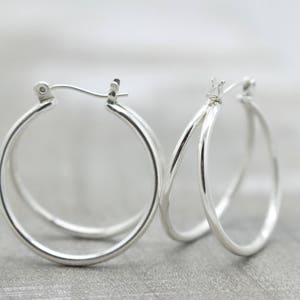 May include: A pair of silver hoop earrings with a double hoop design. The earrings are simple and elegant.