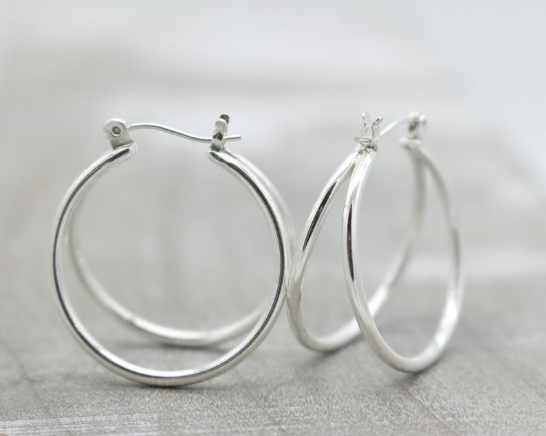 May include: A pair of silver hoop earrings with a double hoop design. The earrings are simple and elegant.