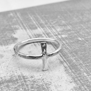 May include: A silver ring with a hammered finish and a cross design.