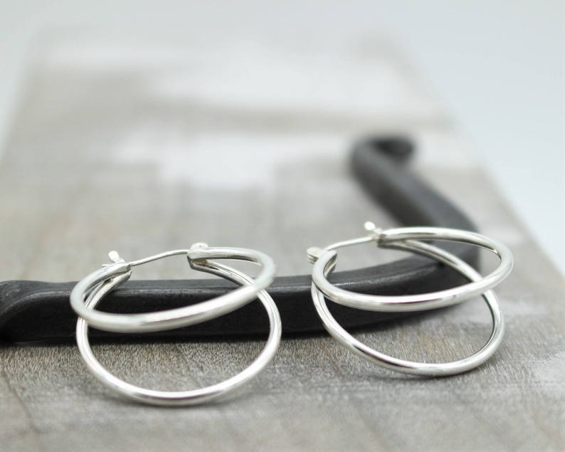 May include: A pair of silver hoop earrings with a double hoop design. The earrings are simple and elegant.