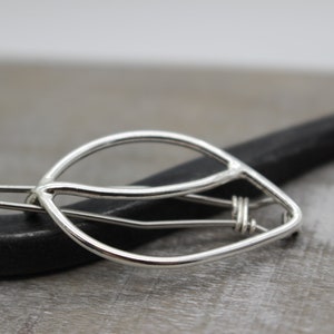 May include: Silver leaf-shaped hair clip with a curved design. The clip is made of wire and has a simple, elegant look.