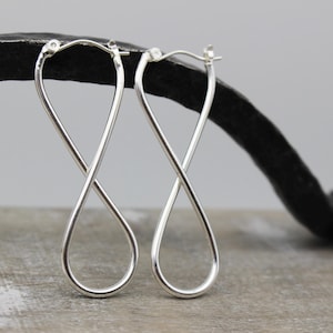 May include: A pair of silver infinity symbol earrings. The earrings are made of a thin, twisted wire and are about 2 inches long.