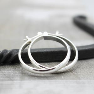 May include: A pair of silver hoop earrings. The earrings are simple and elegant, with a smooth, polished finish.