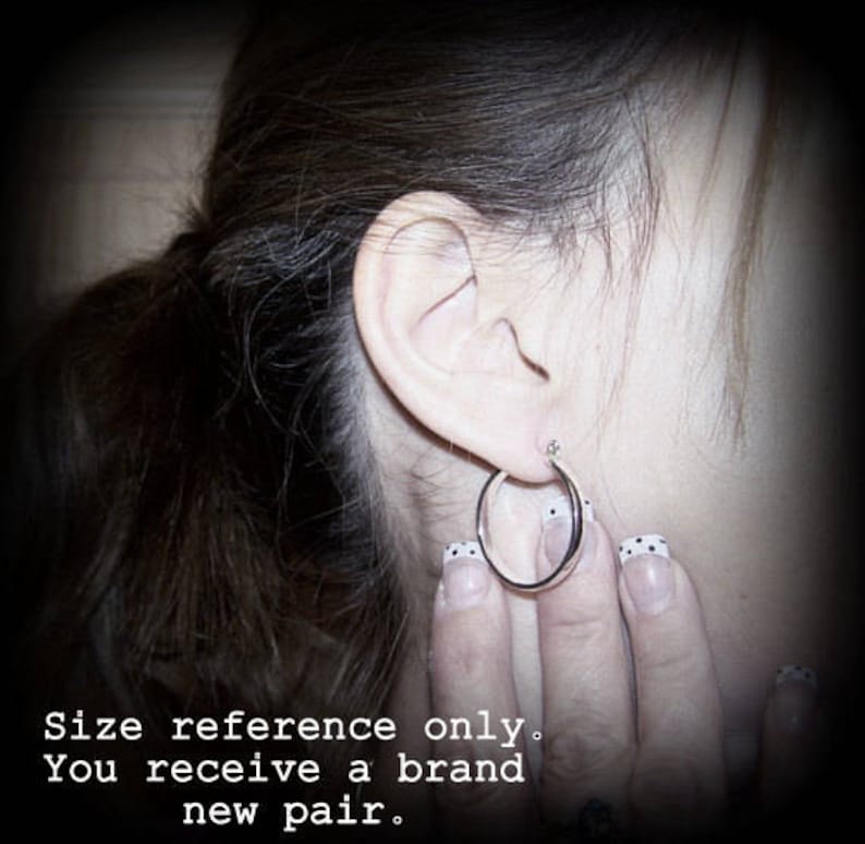 May include: A close-up of a person's ear with a silver hoop earring. The earring is about 1 inch in diameter. The person's hair is dark brown and pulled back in a ponytail.