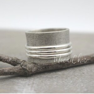 May include: A silver spinning ring with a textured finish and multiple bands. The ring is resting on a branch.