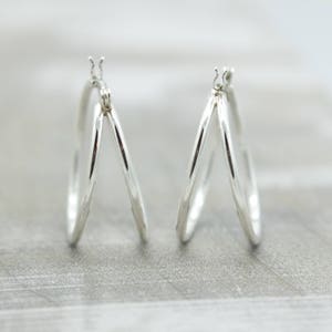 May include: A pair of silver hoop earrings with a triple hoop design. The hoops are smooth and shiny.