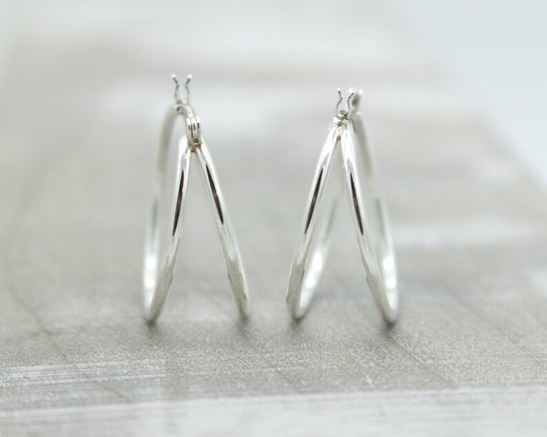 May include: A pair of silver hoop earrings with a triple hoop design. The hoops are smooth and shiny.
