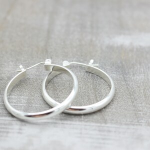 May include: A pair of silver hoop earrings. The earrings are smooth and have a slightly rounded shape.