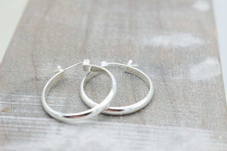 May include: A pair of silver hoop earrings. The earrings are smooth and have a slightly rounded shape.