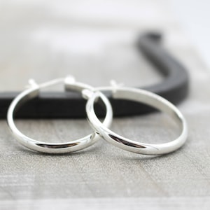 May include: A pair of silver hoop earrings. The earrings are simple and elegant, with a smooth, polished finish.