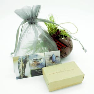 May include: A small, brown box with the word "wish" written on it. The box is sitting on a white surface next to a grey organza bag, a business card, and a small, red and white Christmas bauble.