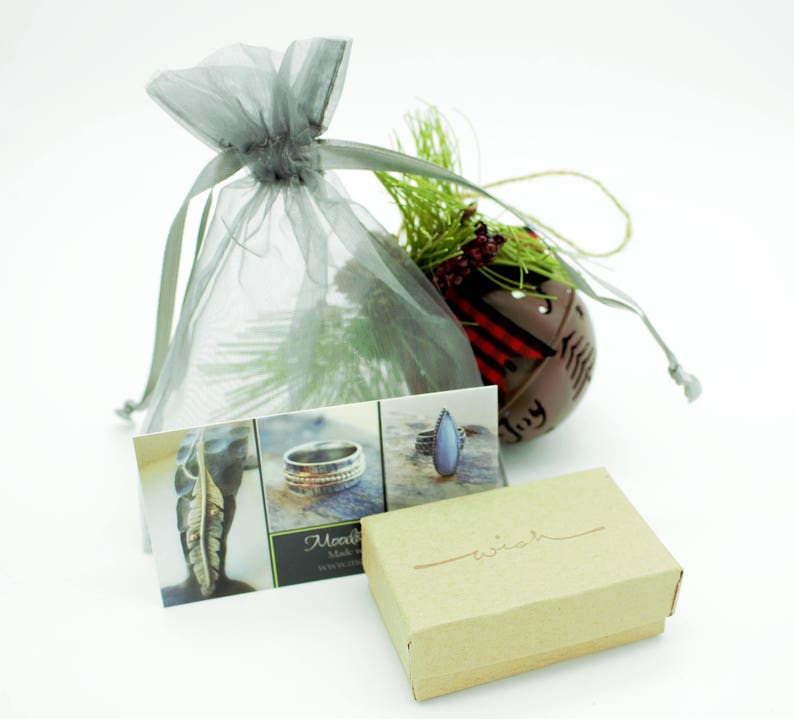 May include: A small, brown box with the word "wish" written on it. The box is sitting on a white surface next to a grey organza bag, a business card, and a small, red and white Christmas bauble.