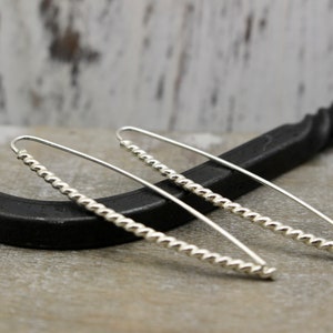 May include: A pair of silver earrings with a twisted, beaded design. The earrings are long and slender, and they hang from the earlobes.