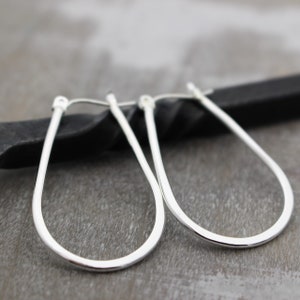 May include: A pair of silver teardrop-shaped hoop earrings. The earrings are made of a thin, smooth metal and have a simple, elegant design.
