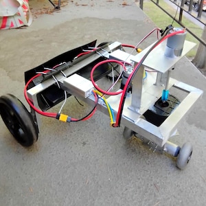 May include: A custom-built robotic chassis featuring a silver metal frame, two large black wheels, and one smaller grey wheel. The device includes exposed electrical wiring in red, black, yellow, and blue, a silver motor, and a black plastic component.