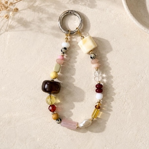 May include: A beaded keychain with a silver clasp. The beads are a mix of shapes and colors, including white, pink, yellow, brown, and clear. Some beads have a speckled pattern. The keychain is likely used for keys or as a decorative accessory.