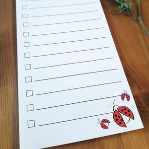 May include: White notepad with black lines and a checklist. The notepad has the words "Things To Do" at the top. The bottom of the notepad has three red ladybugs with black spots.