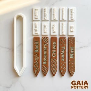 May include: A set of ceramic garden markers and stamps for herbs. The brown markers are embossed with herb names: Basil, Rosemary, Chives, Thyme, and Mint. White stamps include the names of herbs. A white plastic label maker is also included.