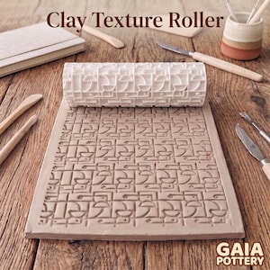 May include: A white cylindrical clay texture roller with a geometric pattern, positioned above a flat slab of light brown clay that displays the same embossed design. The text Clay Texture Roller and GAIA POTTERY are visible.