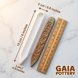 Size reference for Gaia Pottery herb marker clay cutter showing 15cm length and 2cm width beside a finished Basil ceramic marker and wooden ruler for scale