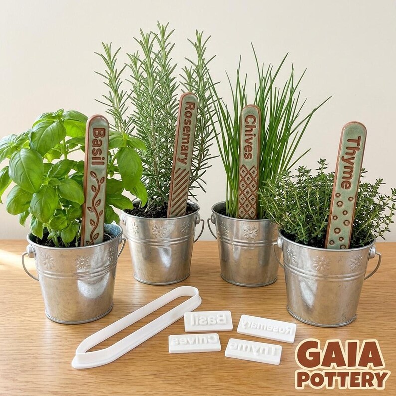 Four galvanized metal herb planters with handmade Gaia Pottery ceramic markers for Basil, Rosemary, Chives and Thyme — made using the clay cutter and stamp set shown beside the pots