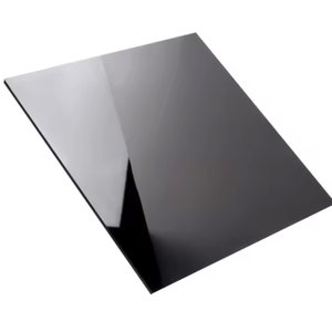 Puede incluir: Una lámina negra rectangular brillante, ligeramente inclinada, que refleja la luz. La superficie es lisa y pulida, con un acabado oscuro similar a un espejo. Los bordes son limpios y afilados.