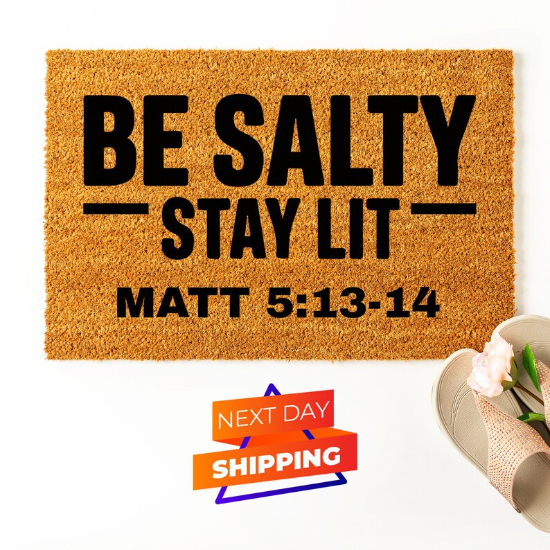May include: A brown doormat with the text "BE SALTY - STAY LIT - MATT 5:13-14" in black lettering.