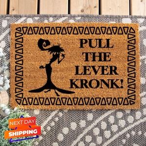 May include: A rectangular doormat made of natural coir fiber. The mat features a black silhouette of a character and the phrase "PULL THE LEVER KRONK!" in black block letters. The border is decorated with black triangles.