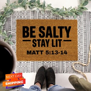 May include: A brown doormat with the text "BE SALTY - STAY LIT - MATT 5:13-14" in black.