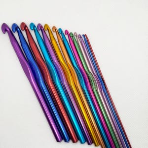 Puede incluir: Un juego de 14 agujas de crochet de colores, dispuestas en un patrón de arcoíris, con las puntas de las agujas mirando hacia el lado derecho de la imagen.