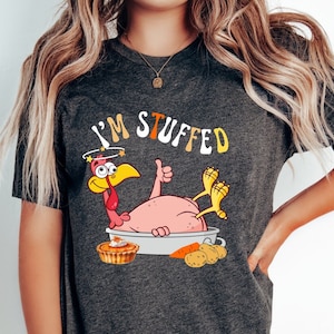 Pode incluir: Uma camiseta cinza com um peru de desenho animado com uma expressão tonta e o texto "I'M STUFFED".