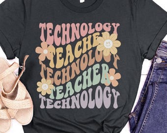 May include: Dark heather grey t-shirt with a retro-style graphic that says "Technology Teacher" in colorful, wavy letters with flowers and smiley faces.
