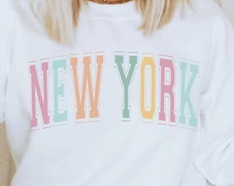 May include: White sweatshirt with a colorful "NEW YORK" graphic printed on the front.
