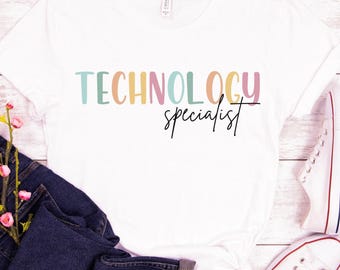 May include: White t-shirt with the text "TECHNOLOGY specialist" in colourful letters. The shirt is on a white wooden background with blue jeans and white trainers.