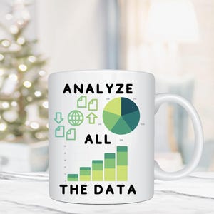 Puede incluir: Taza de café de cerámica blanca con un diseño en negro y verde. La taza tiene el texto "Analyze All The Data" y presenta un gráfico circular y un gráfico de barras.